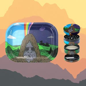 May include: A rolling tray and grinder set with a cartoon Bigfoot design. The tray shows a landscape with a rainbow, and the grinder has several sections. The colour scheme includes blue, green, and purple. The set is designed for rolling herbs.