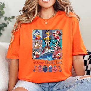 Puede incluir: Camiseta naranja con un dise&ntilde;o colorido de personajes de Disney, incluyendo Mickey Mouse, Minnie Mouse, Donald Duck y Goofy, dispuestos en una cuadr&iacute;cula. El dise&ntilde;o incluye un crucero y el texto "Disney Cruise Line".