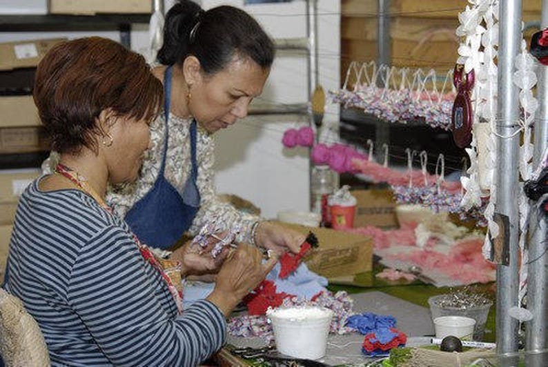 May include: Two people are working on a craft project. One person is holding a blue and white flower and the other person is holding a red and white flower. There are many other flowers in the background.