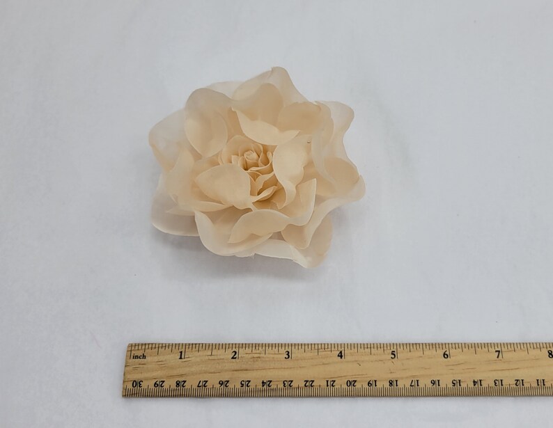 May include: A large, peach-colored fabric flower with multiple layers of petals. The flower is approximately 2 inches in diameter.