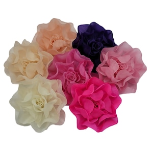 May include: Six large fabric flowers in various shades of pink, peach, and purple. The flowers are made of soft, ruffled fabric and have a realistic appearance.