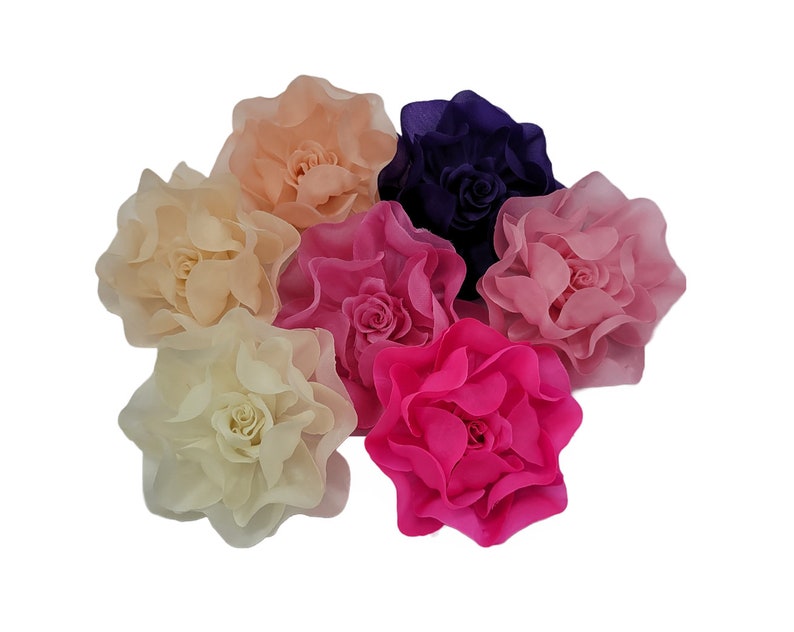 May include: Six large fabric flowers in various shades of pink, peach, and purple. The flowers are made of soft, ruffled fabric and have a realistic appearance.