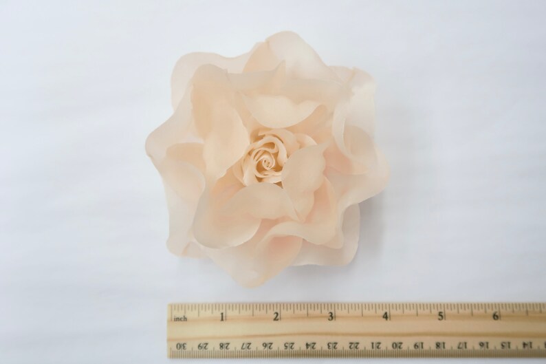 May include: A large, peach-colored fabric rose with a ruffled texture. The rose is approximately 4 inches in diameter.