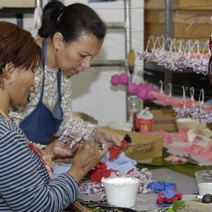 Peut inclure: Deux femmes travaillent sur des projets artisanaux. L'une porte une chemise ray&eacute;e, l'autre un haut fleuri et un tablier en jean. Elles sont entour&eacute;es de mat&eacute;riaux, notamment des fleurs, du tissu et des r&eacute;cipients. La sc&egrave;ne sugg&egrave;re un atelier.