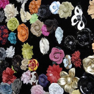 May include: A collection of colorful fabric flowers in various shapes and sizes. The flowers are made of leather, velvet, and other materials. They are arranged on a black background.