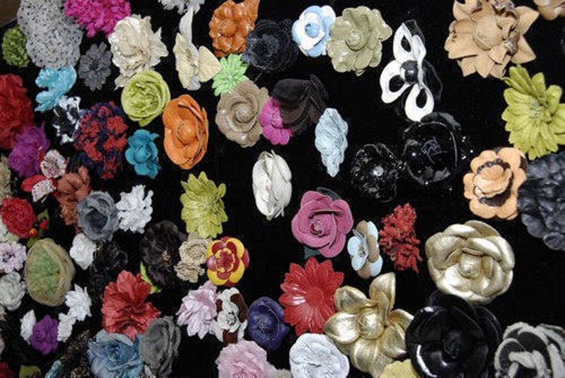 May include: A collection of colorful fabric flowers in various shapes and sizes. The flowers are made of leather, velvet, and other materials. They are arranged on a black background.