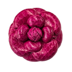 以下が含まれることがあります： 表面がテクスチャ加工された、濃いピンク色の革製の大きな花の形をしたブローチです。