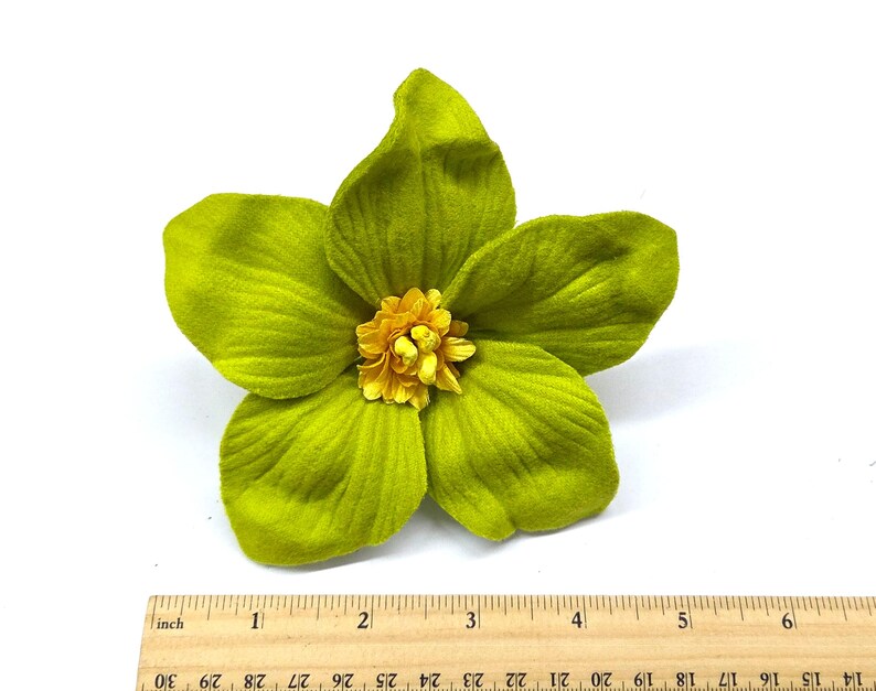 Peut inclure: Une grande fleur artificielle avec cinq p&eacute;tales vert lime et un centre jaune. Les p&eacute;tales ont une texture velout&eacute;e. Une r&egrave;gle en bois avec des marquages en pouces est au bas de l'image.