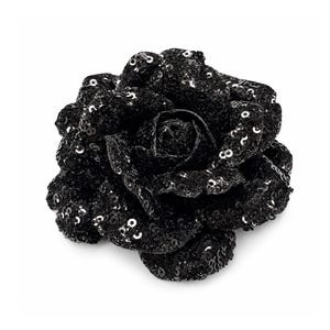 Può includere: Un accessorio a forma di rosa nera ricoperto di piccole paillettes nere riflettenti. Il fiore presenta molteplici petali stratificati che creano una forma piena e arrotondata, con le paillettes che catturano la luce per un aspetto testurizzato.