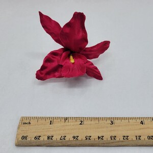May include: A single, deep red silk orchid flower with a yellow center. The flower is approximately 2 inches wide.
