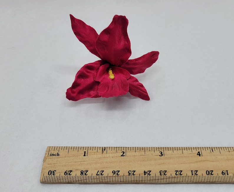 May include: A single, deep red silk orchid flower with a yellow center. The flower is approximately 2 inches wide.