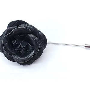 Può includere: Una spilla da bavero in pelle nera a forma di rosa con uno spillo argentato.