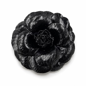May include: A black flower-shaped accessory crafted with a textured, scale-like pattern resembling snakeskin. The object features multiple overlapping, rounded petals arranged in a circular, layered formation, creating a dimensional, bloom-like appearance.