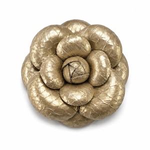 May include: A gold-colored brooch shaped like a multi-layered flower. The petals have a textured, scale-like surface finish. The central part of the flower is composed of tightly arranged, rounded petals, while the outer layers are larger and curved.