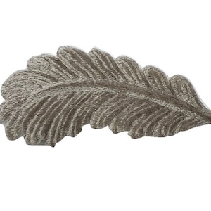 May include: A detailed, silver-colored leaf-shaped decorative element. The leaf has a textured surface with visible veins and a curved shape, set against a plain white background. This item could be used for crafting or home decor.
