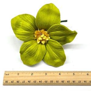 Peut inclure: Une grande fleur artificielle avec cinq p&eacute;tales chartreuse et un centre jaune. La fleur mesure environ 13 cm de diam&egrave;tre. Une tige verte est visible. Une r&egrave;gle en bois est plac&eacute;e en dessous.