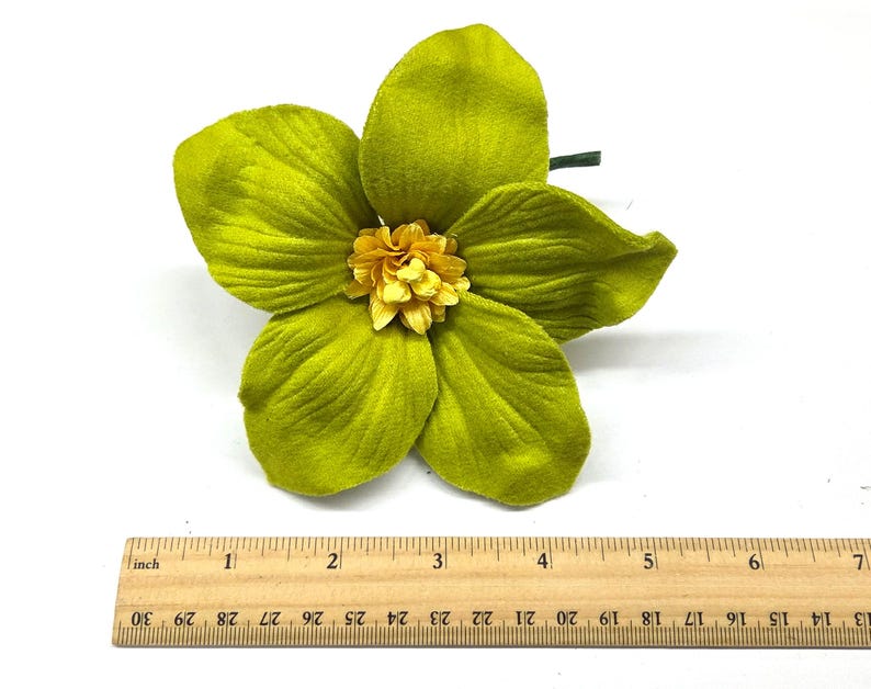 Peut inclure: Une grande fleur artificielle avec cinq p&eacute;tales chartreuse et un centre jaune. La fleur mesure environ 13 cm de diam&egrave;tre. Une tige verte est visible. Une r&egrave;gle en bois est plac&eacute;e en dessous.