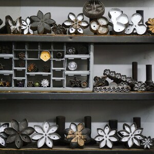 May include: A shelf with a variety of metal flower-shaped cookie cutters, some in a drawer, some on the shelf. There is a red fire extinguisher on the right side of the shelf.