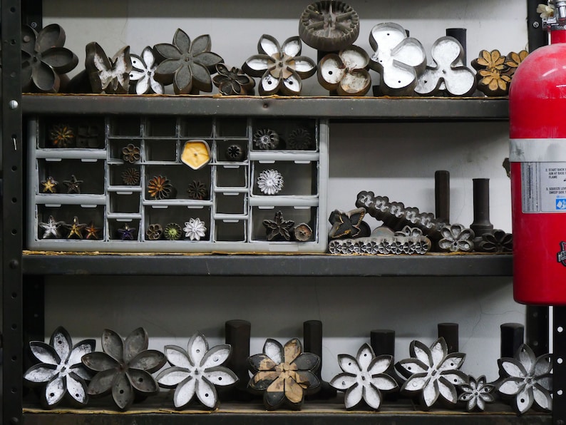 May include: A shelf with a variety of metal flower-shaped cookie cutters, some in a drawer, some on the shelf. There is a red fire extinguisher on the right side of the shelf.