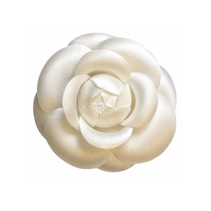 Peut inclure: Une broche fleur de camélia blanche avec une finition lisse et satinée. L'accessoire présente de multiples pétales arrondis et superposés, disposés en un motif circulaire et étagé qui rayonne à partir d'un centre replié.
