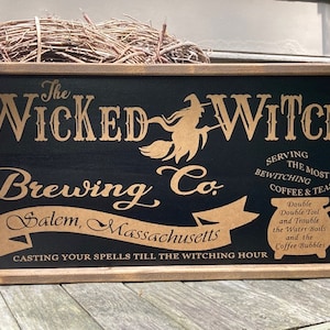 May include: Wooden framed sign with the text "The Wicked Witch Brewing Co." in gold lettering on a black background. The sign includes a witch silhouette and the phrase "Serving the Most Bewitching Coffee & Teas."