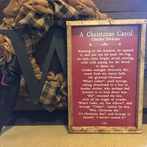 Peut inclure: Une impression encadr&eacute;e avec un fond rouge et du texte blanc. Le texte est un extrait de "Un chant de No&euml;l" de Charles Dickens. Le cadre est en bois avec une finition rustique.