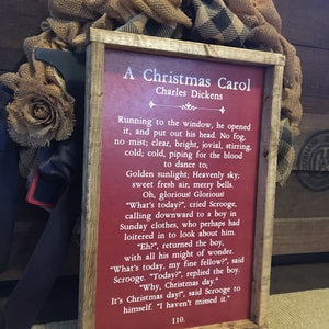 Peut inclure: Une pancarte en bois rouge avec une bordure blanche et du texte blanc. La pancarte indique "A Christmas Carol" de Charles Dickens. Le texte se poursuit avec un extrait du livre, d&eacute;crivant un matin de No&euml;l lumineux et froid.