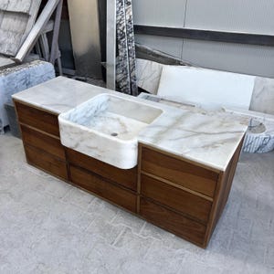 Puede incluir: Un mueble de ba&ntilde;o hecho a medida con encimera de m&aacute;rmol y lavabo integrado. El mueble cuenta con un mueble de madera c&aacute;lida con m&uacute;ltiples cajones y una pila de m&aacute;rmol. El m&aacute;rmol tiene vetas grises.