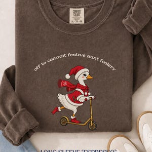 May include: A dark brown long-sleeve crewneck sweatshirt featuring a graphic of a white goose wearing a red Santa hat and scarf while riding a yellow scooter. The text above the goose reads, off to commit festive aunt foolery.