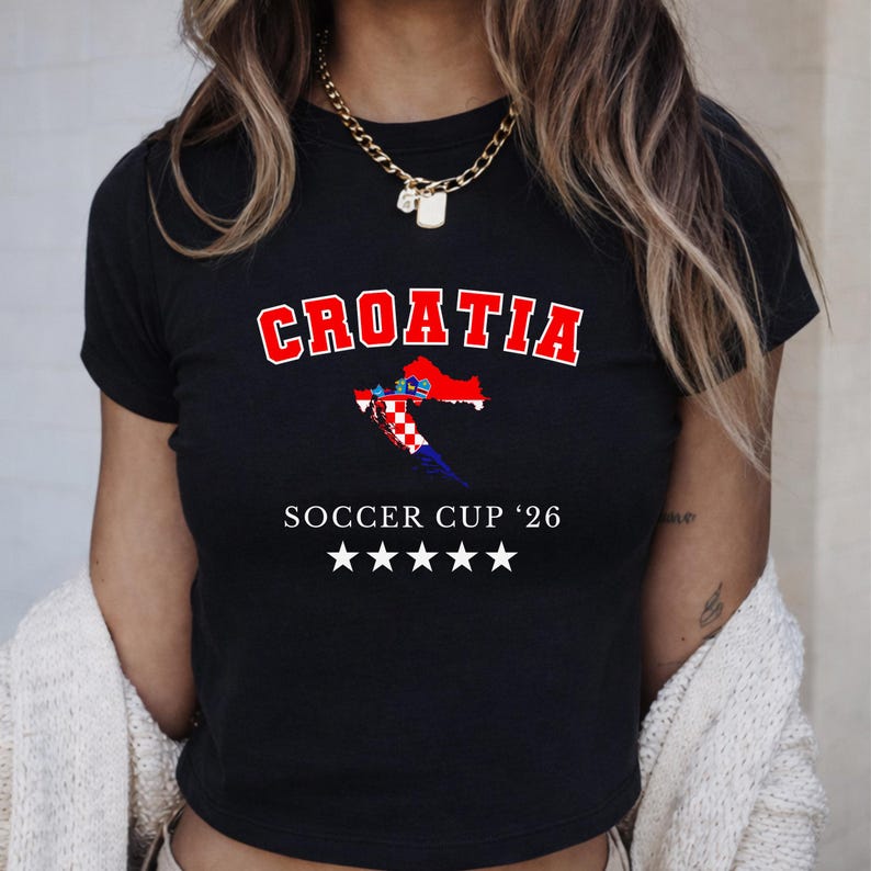 Close-up of a black Croatia soccer baby tee on a model. The design elements, including the five stars and flag-filled map, are displayed with high-contrast, moody lighting.