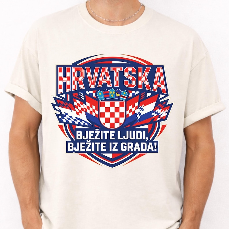 May include: Cream-colored t-shirt featuring a graphic design with the word "HRVATSKA" in red and white checkered letters. Below, a crest and the text "BJEŽITE LJUDI, BJEŽITE IZ GRADA!" are displayed in blue and red.