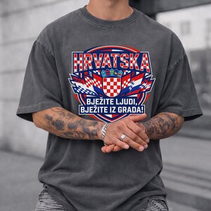 Dark charcoal gray vintage washed t-shirt featuring a large Croatia soccer graphic with red-white checkered shield coat of arms, flags, and bold "HRVATSKA" typography print on a tattooed man.