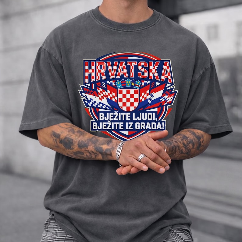 Dark charcoal gray vintage washed t-shirt featuring a large Croatia soccer graphic with red-white checkered shield coat of arms, flags, and bold "HRVATSKA" typography print on a tattooed man.