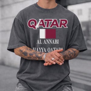 Pepper T-shirt featuring maroon Qatar typography, national flag, and Al Annabi football fan design.