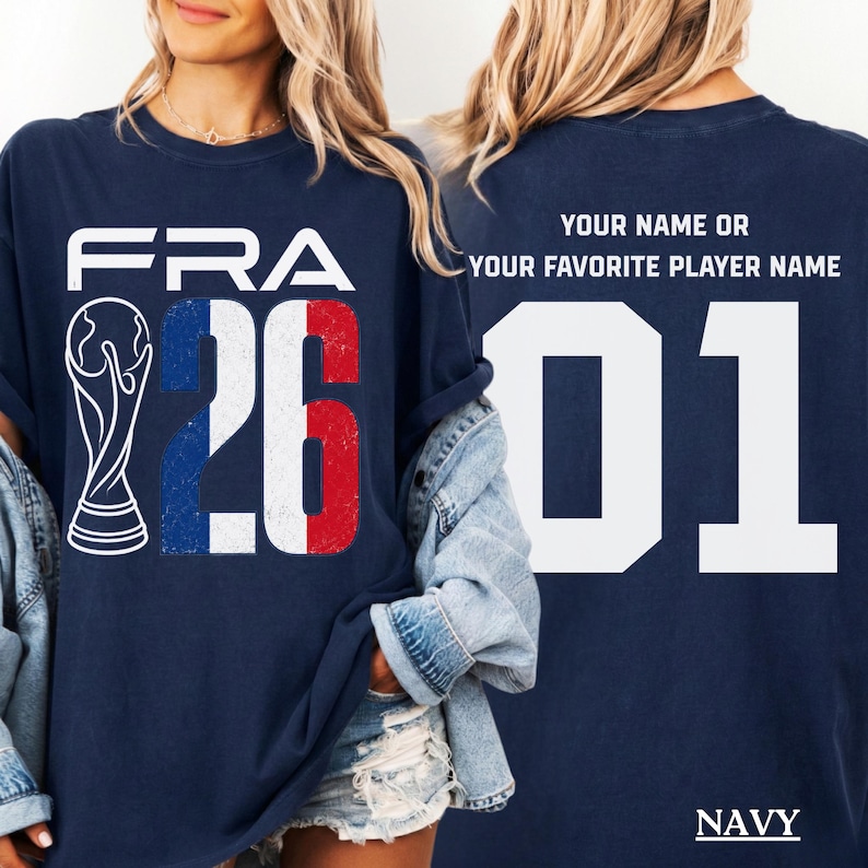 Split-view lifestyle mockup of a blonde female model in a navy blue t-shirt with a denim jacket hanging loosely off her shoulders. The left panel shows the front design containing the white "FRA" text and tricolor "26" details next to a white world championship cup illustration. The right panel shows the back layout featuring the customizable text template placeholder "YOUR NAME OR YOUR FAVORITE PLAYER NAME 01".