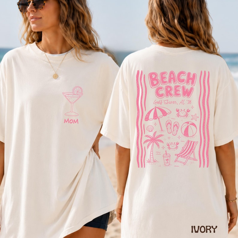 May include: An ivory t-shirt featuring a pink graphic of a cocktail glass and the word MOM on the front left chest. The back displays a large pink graphic with the text BEACH CREW, Gulf Shores, AL '26, surrounded by beach icons like a palm tree.