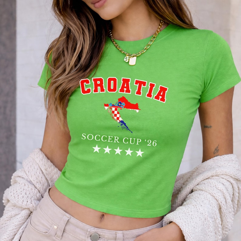 May include: A lime green crop top with the word "CROATIA" in red block letters above a map of Croatia. Below the map is the text "SOCCER CUP '26" and five white stars. The shirt is short-sleeved.
