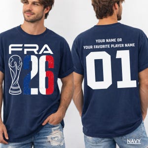 Puede incluir: Camiseta azul marino con "FRA 26" en blanco, rojo y azul, con un gr&aacute;fico de trofeo. La parte trasera de la camiseta muestra "TU NOMBRE O EL NOMBRE DE TU JUGADOR FAVORITO" encima del n&uacute;mero "01" en blanco. La palabra "MARINO" est&aacute; en la parte inferior.