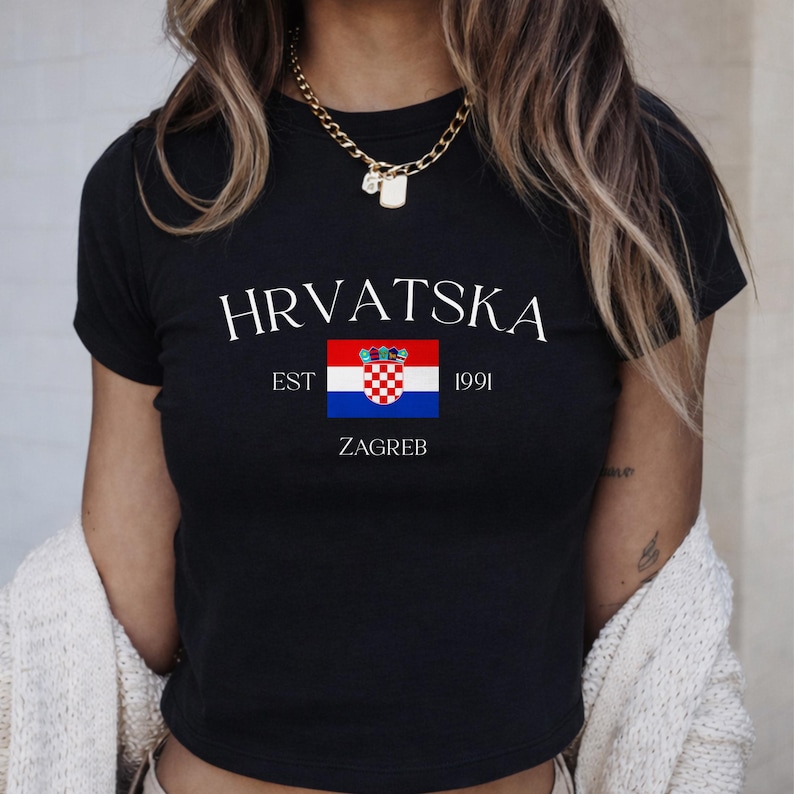 May include: Black t-shirt with the word "HRVATSKA" in white, above a Croatian flag graphic. Below the flag are the words "EST 1991 ZAGREB". The shirt has short sleeves and a crew neck.