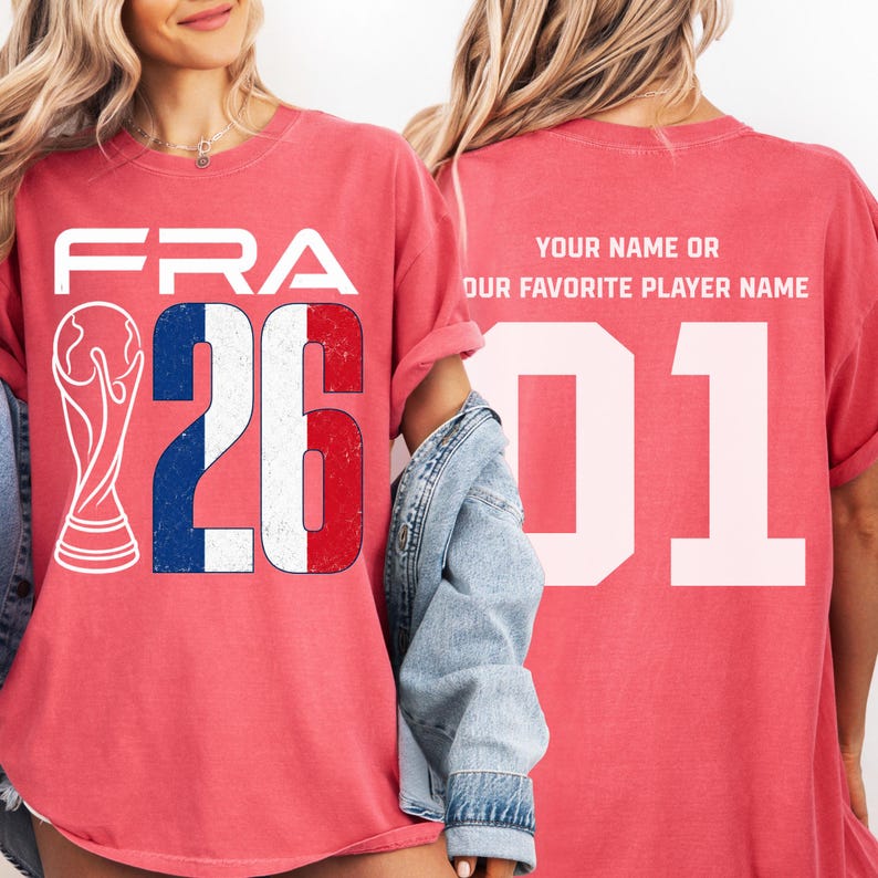Puede incluir: Camiseta roja con "FRA" y el n&uacute;mero "26" en blanco, con la bandera francesa incorporada en el dise&ntilde;o. Un gr&aacute;fico blanco de un trofeo est&aacute; a la izquierda. La parte trasera de la camiseta tiene el n&uacute;mero "01" y texto.