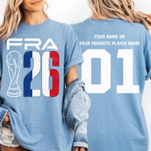 Puede incluir: Camisetas de color azul claro con un dise&ntilde;o de la bandera francesa. La parte delantera de la camiseta muestra "FRA" encima del n&uacute;mero "26" con los colores de la bandera francesa. La parte trasera de la camiseta tiene el n&uacute;mero "01" y el texto "YOUR NAME OR YOUR FAVORITE PLAYER NAME".