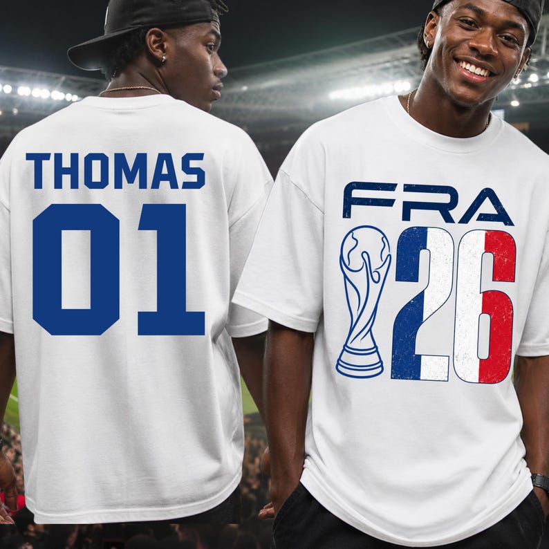 Front and back split preview featuring two male models in a brightly lit stadium environment. The model on the right smiles while facing forward, displaying the white graphic t-shirt with a distressed French flag texture inside the "26" block numbers. The model on the left is turned back, showing the personalized text layout "THOMAS 01" printed cleanly across the shoulders.