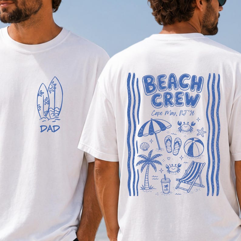 May include: A white t-shirt featuring blue ink graphics. The front shows two surfboards and the word DAD. The back displays the text BEACH CREW Cape May, NJ '26, surrounded by illustrations of a beach umbrella, palm tree, chair, and crabs.