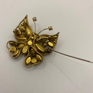 May include: Gold tone butterfly brooch with rhinestones. The brooch has a pin back and is marked "Belleair".