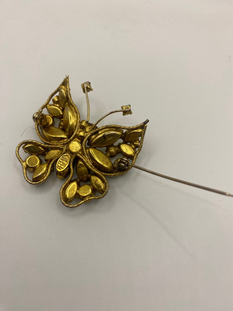 May include: Gold tone butterfly brooch with rhinestones. The brooch has a pin back and is marked "Belleair".