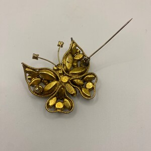 May include: Gold tone butterfly brooch with rhinestones. The brooch has a pin back.