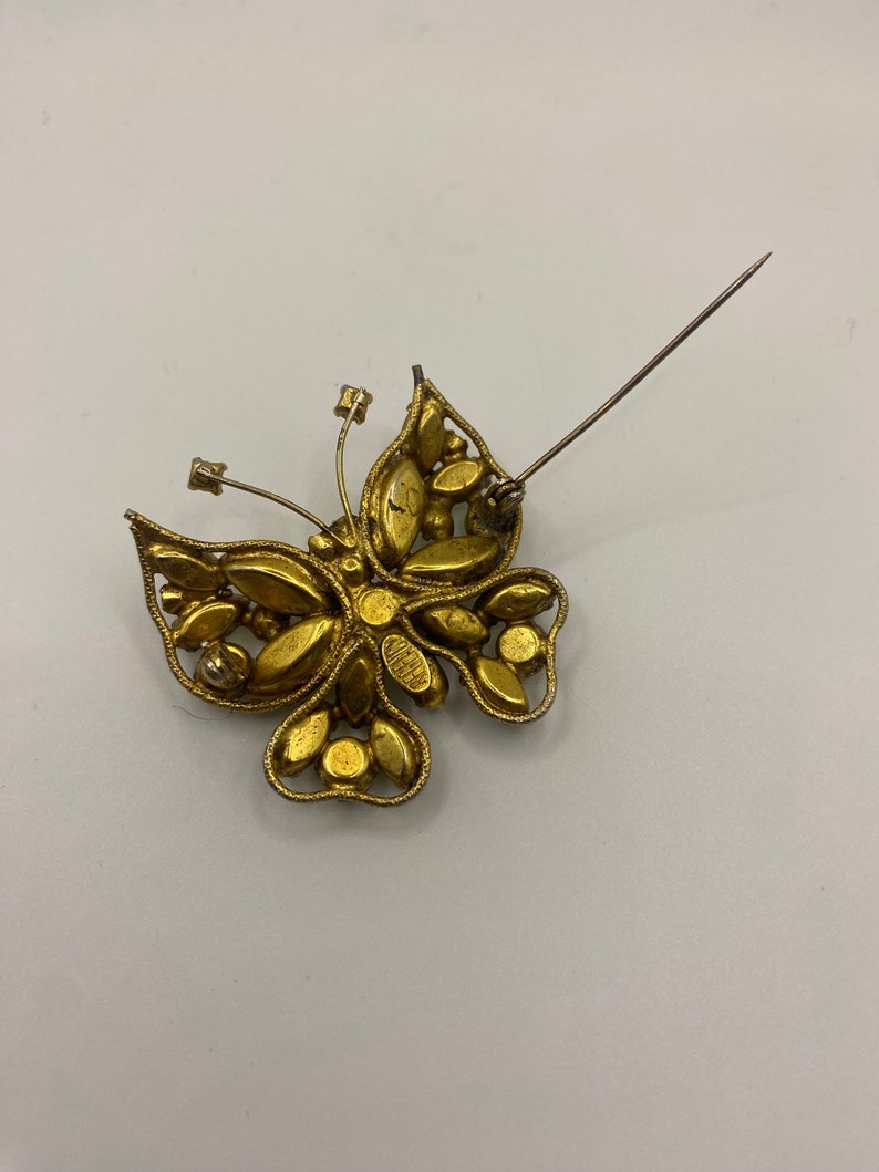 May include: Gold tone butterfly brooch with rhinestones. The brooch has a pin back.