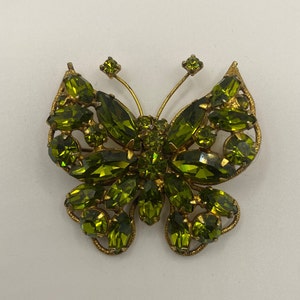 May include: A gold-tone butterfly brooch with green rhinestones. The butterfly has a detailed design and is a vintage style.