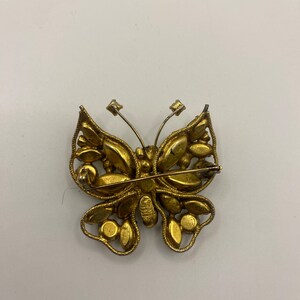 May include: A gold-toned butterfly brooch with clear rhinestones. The brooch has a pin and catch closure on the back.