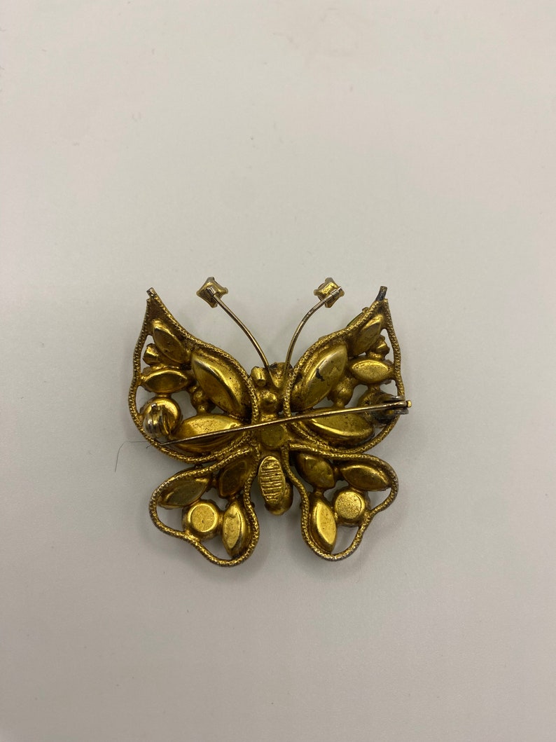 May include: A gold-toned butterfly brooch with clear rhinestones. The brooch has a pin and catch closure on the back.